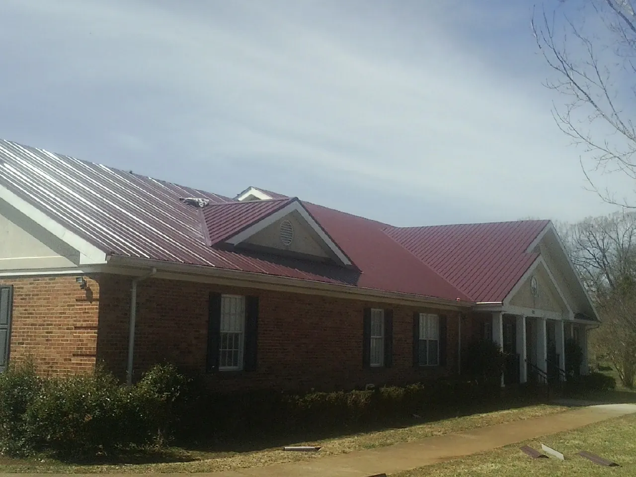 Red metal roof with gabled entries on a long brick building, from a Hail Damage Roof Repair job in Dorchester