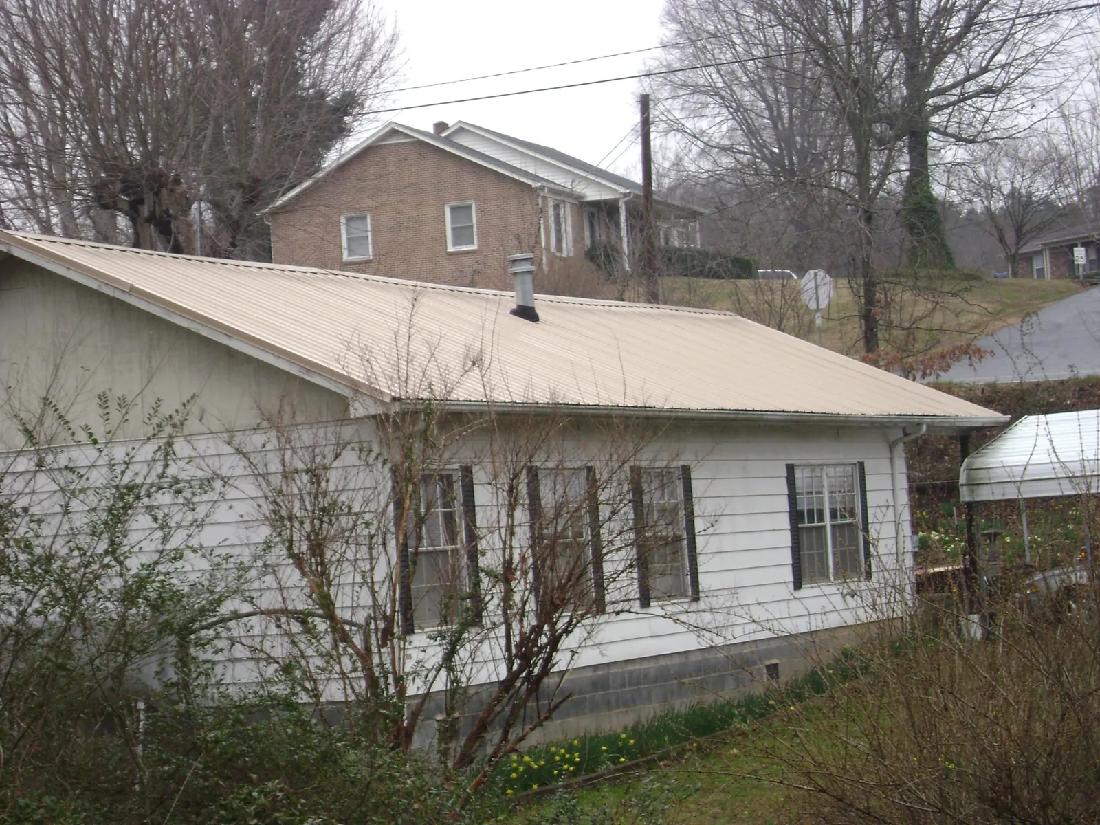 Tan metal roof on a white sided house set into a hillside — Commercial Roofing by Roofing Brothers in Dorchester