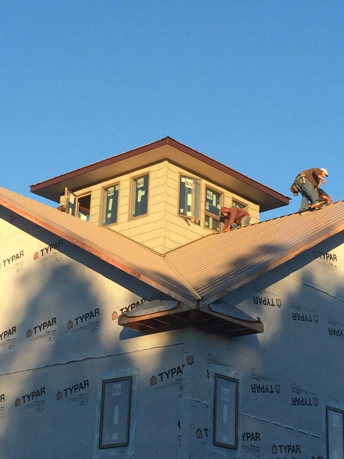 Roofers working around a rooftop cupola on a new metal roof at sunset — Roof Waterproofing in Dorchester by Roofing Brothers